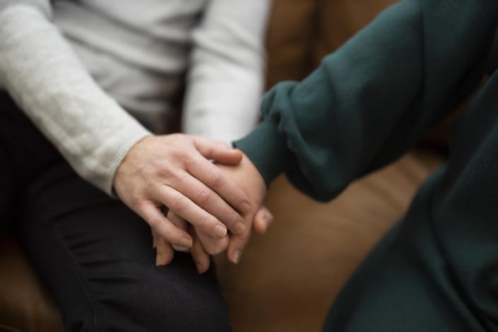 to mennesker holder i h&aring;nd siddende i sofa